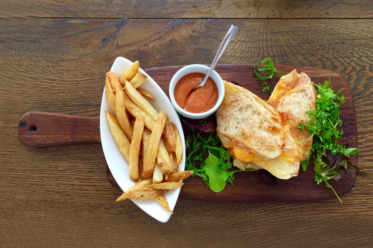 Delicious grilled cheese sandwich with crispy fries and a side of dipping sauce on a wooden table.