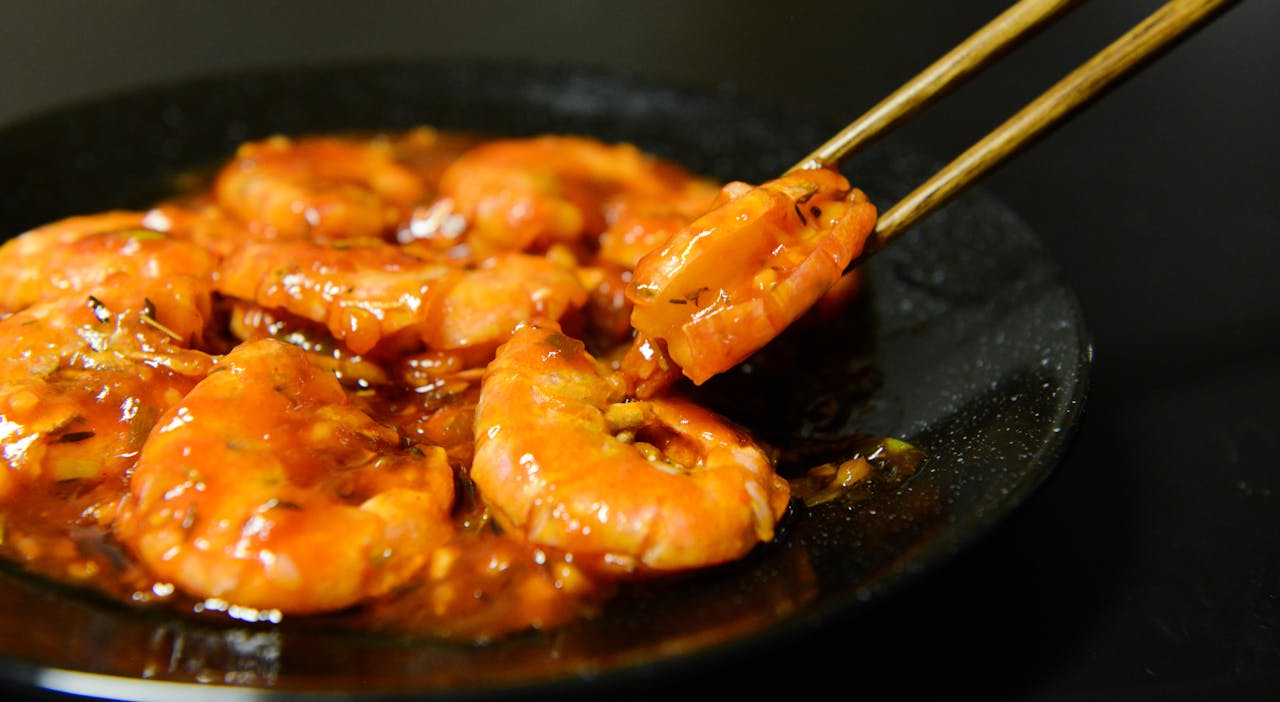 Close-up of spicy prawns in sauce with chopsticks on a dark plate